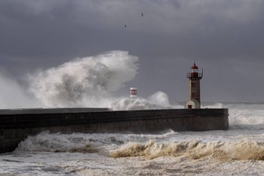 Rıhtımlar üzerinde büyük beyaz dalgalar ve deniz feneri yağmurdan önce kara bulutlu bir gökyüzüne karşı. Douro nehri ağzı, Porto, Portekiz, deniz fırtınası sırasında.