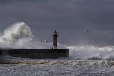 Rıhtımlar üzerinde büyük beyaz dalgalar ve deniz feneri yağmurdan önce kara bulutlu bir gökyüzüne karşı. Douro nehri ağzı, Porto, Portekiz, deniz fırtınası sırasında.