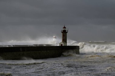 Rıhtımlar üzerinde büyük beyaz dalgalar ve deniz feneri yağmurdan önce kara bulutlu bir gökyüzüne karşı. Douro nehri ağzı, Porto, Portekiz, deniz fırtınası sırasında.
