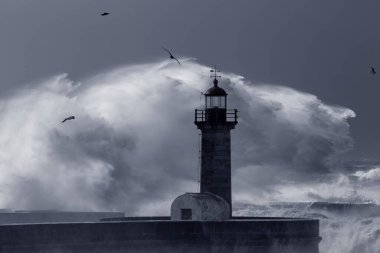 Büyük deniz dalgalarının Douro nehrinin ağzına sıçradığını gören kara fırtına. Eski deniz feneri ve iskele, Porto, Portekiz. Ton mavisi