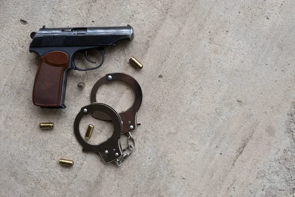 traumatic metal gun for self defence with 9 mm bullets and a handcuffs on a gray concrete background. top view, flat lay, copy space