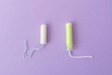 Açık yeşil aplikatörlü ve mor arka planda aplikatörsüz iki pamuk tampon. Hijyenik tampon çeşitleri. Adet, koruma, karşılaştırma kavramı, düz yatıyordu, Kopyalama alanı, üst görünüm