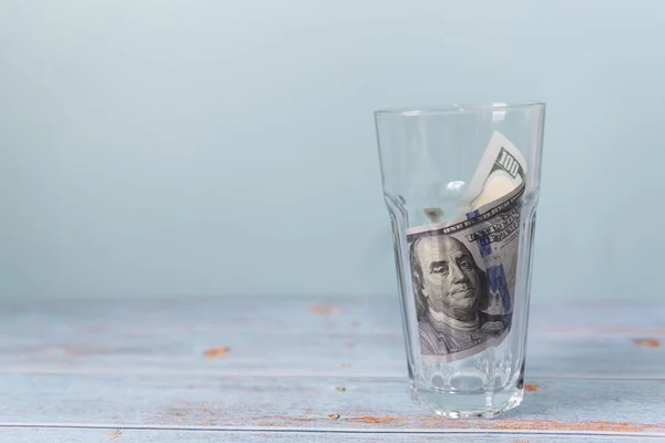 100 banknot, ahşap bir masa ve mavi bir zemin üzerindeki bardakta toplandı. Boşluğu kopyala, para biriktirme kavramı