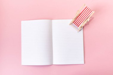Boş defter, pembe arka planda bir şezlong modeliyle açıldı. Tatil planlama konsepti. Turizm. Minimalizm. Düz yat, boşluğu kopyala.