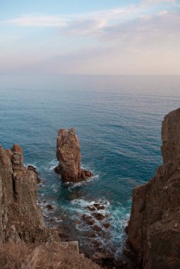 Uçurumun tepesinden bakan güzel deniz ve kayalar. Atardamar gözünden çeşitli deniz köpüğü dalgaları. Akşam ışığı, temiz şeffaf su, Primorye, Uzak Doğu, Rusya