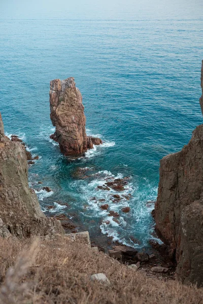 Uçurumun tepesinden bakan güzel deniz ve kayalar. Atardamar gözünden çeşitli deniz köpüğü dalgaları. Akşam ışığı, temiz şeffaf su, Primorye, Uzak Doğu, Rusya