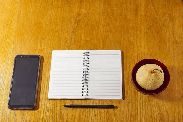 Flach lag minimalistischer Arbeitsplatz. Schreibtisch aus Holz mit Notizbuch, Stift und Obst. — Stockfoto