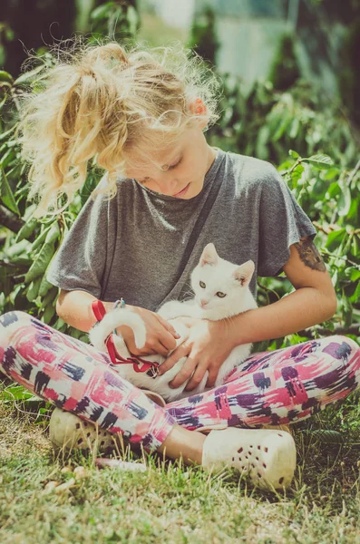 可爱的金发女孩和白猫坐在一起户外在花园里 — 图库照片