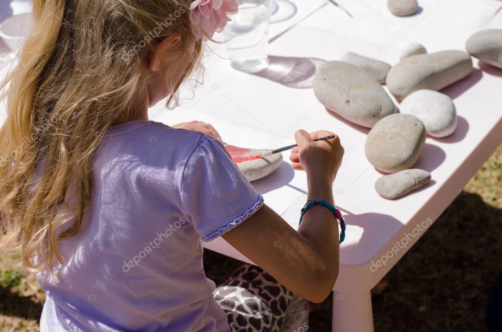 cute little blond girl with long hair having fun painting stones