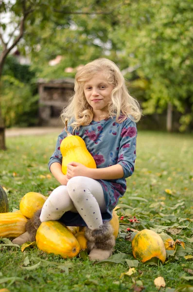 緑の秋の庭にオレンジ色のカボチャと美しいブロンドの女の子 — ストック写真