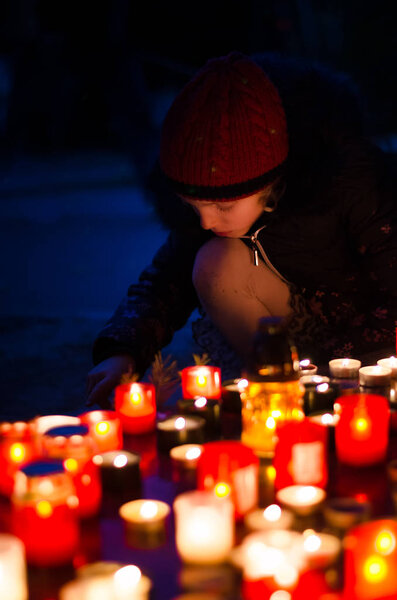 child burning candle during  All Saints Day at the cemetery at dark night 