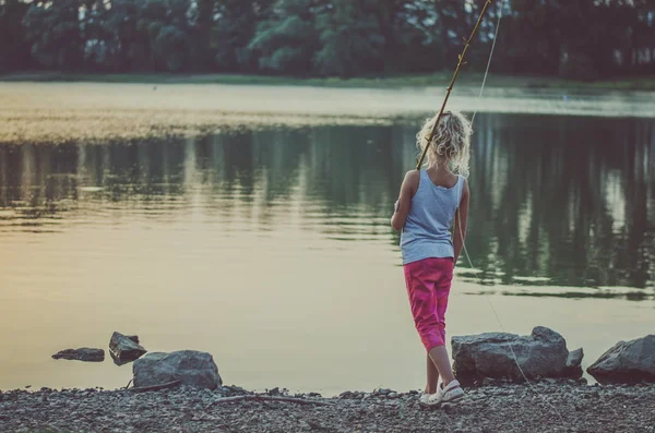 日没時の池で自家製釣り竿で愛らしい小さな女の子の釣り — ストック写真