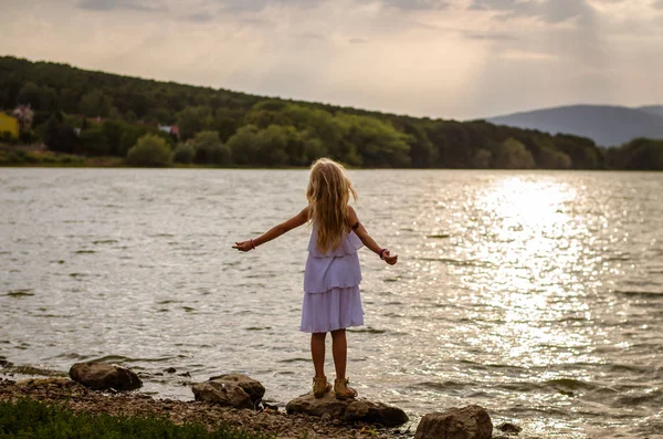 バックの夕景でリラックスした午後の屋外池でドレスの愛らしい少女 — ストック写真