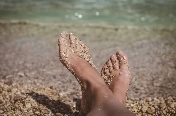 海辺のビーチで小さな石で覆われた足を見る — ストック写真