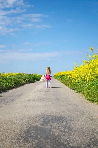 Bambino piccolo che cammina vicino campo di colza sotto il cielo blu — Foto Stock