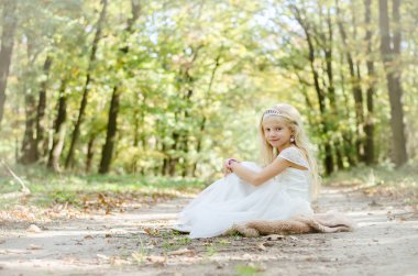 ağaçların altında prenses elbisesi içinde oturan romantik çocuk