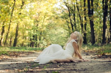 ağaçların altında prenses elbisesi içinde oturan romantik çocuk