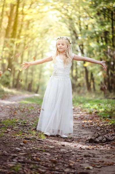 Adorable blond girl with leaves in hands in sunny day in magical forest — Stock Photo, Image