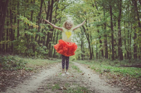 Adorável loira menina em laranja tutu saia saltando na floresta — Fotografia de Stock