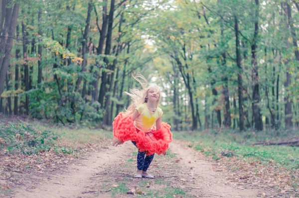 Bedårande blond flicka i orange tutu kjol hoppa i skogen — Stockfoto