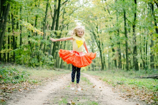 Schattig blond meisje in oranje tutu rok springen in bos — Stockfoto