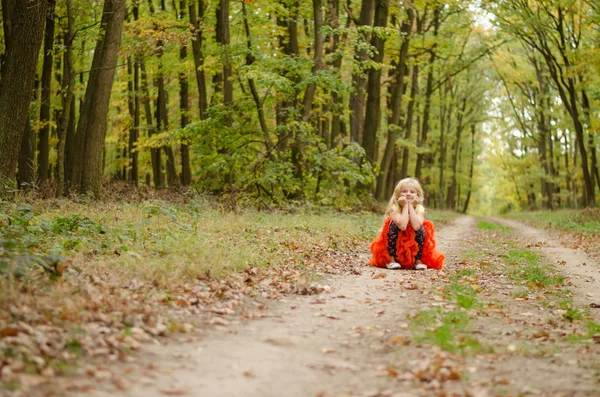 Rozkošná blond dívka v oranžové sukně sedí na venkově cestu v lese — Stock fotografie