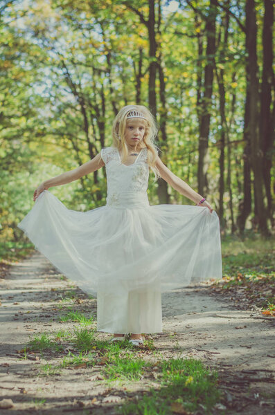Cute little girl in long white wedding dress posing in magic forest