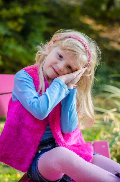Little sad child sitting in pink bench in beautiful nature — Stock Photo, Image