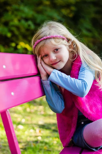 Pequeño niño triste sentado en el banco rosa en la hermosa naturaleza — Foto de Stock