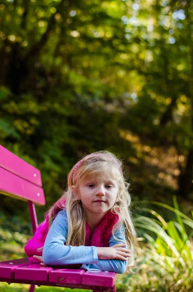 Klein droevig kind zittend in roze bankje in prachtige natuur — Stockfoto