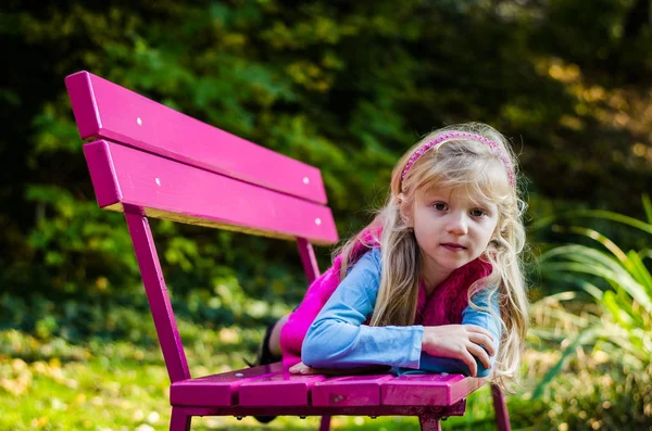 Little sad child sitting in pink bench in beautiful nature — Stock Photo, Image