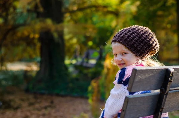 Piccolo bambino triste seduto in panchina di legno nella bella natura — Foto Stock