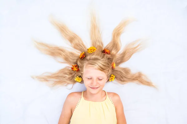 Adorable enfant souriant avec des cheveux blonds longs sains et forts en forme de soleil orné de fleurs copier l'espace les yeux fermés — Photo