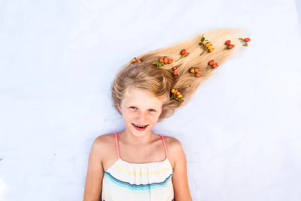 Okouzlující usměvavé dítě se zdravými a silnými dlouhými blond vlasy ve tvaru táboráku s květinovým aranžmá — Stock fotografie