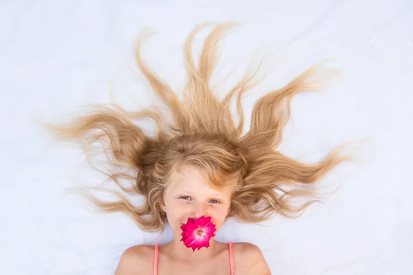 Charming smiling child with healthy and strong long blond hair and red rose flower in mouth — Stock Photo, Image