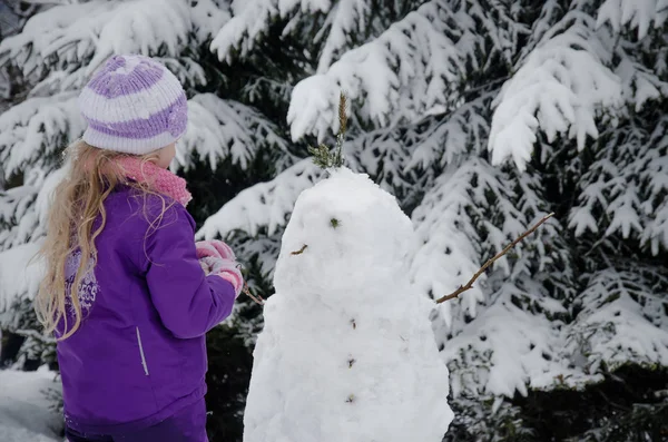 Sevimli genç çocuk kışın çok kar ve küçük kardan adamla eğleniyor. — Stok fotoğraf