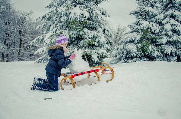 Child having happy winter time with lot of snow and little snowman built in sleight — Stock Photo, Image