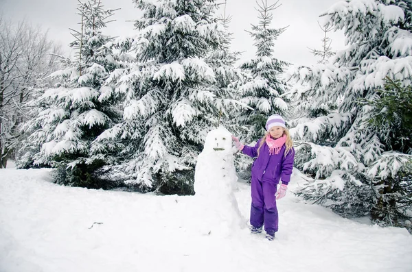 Niño, muñeco de nieve y bosque de invierno — Foto de Stock