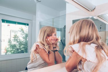 Çekici sarışın kız aynanın önünde gülümsüyor ve düşünüyor.