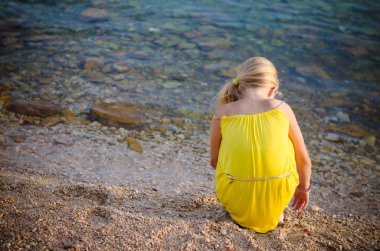 Denizin kıyısındaki kayalık sahilde çakıl taşlarıyla oynuyorlar.