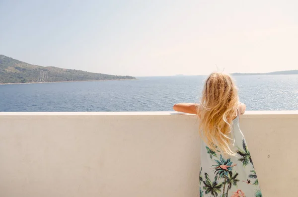 Bedårande flicka med långt blont hår och sommarklänning tittar från balkongen — Stockfoto