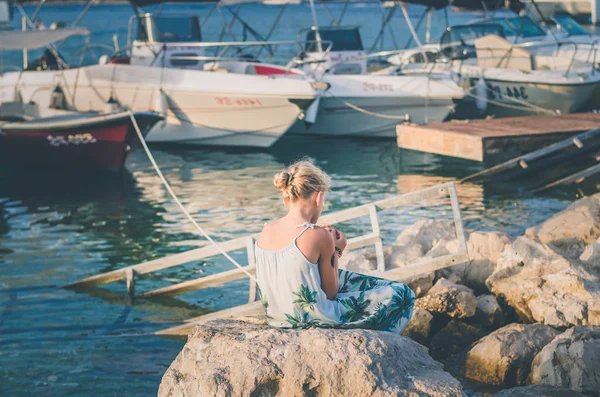 Criança pequena sozinha sentada na grande pedra na costa do mar — Fotografia de Stock