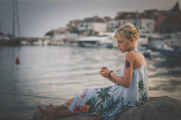 Criança pequena sozinha sentada na grande pedra na costa do mar — Fotografia de Stock