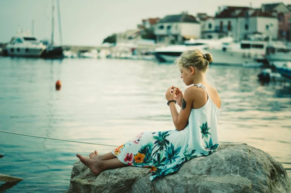 Criança pequena sozinha sentada na grande pedra na costa do mar — Fotografia de Stock