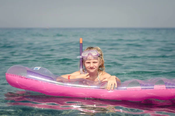 与金发碧眼的女孩在蔚蓝的大海中享受假期 躺在橡胶粉色的气垫上 快乐地微笑着的孩子 — 图库照片