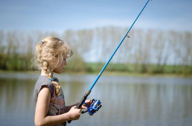 Küçük sarışın çocuk balık tutuyor. Doğal gölde olta ile balık tutuyorlar.