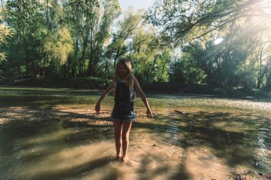 Aktif kız, romantik yeşil parkta altın saatinde sığ nehirde eğleniyor.