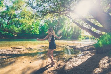 Aktif kız, romantik yeşil parkta altın saatinde sığ nehirde eğleniyor.