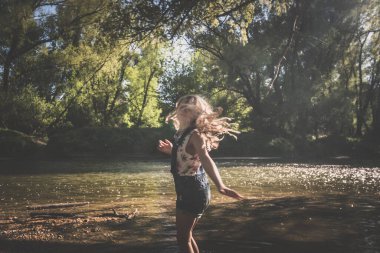 Aktif kız, romantik yeşil parkta altın saatinde sığ nehirde eğleniyor.