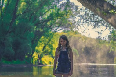 Romantik yeşil bir ortamda, altın saatinde hala çocuk. Etrafında nehir var.